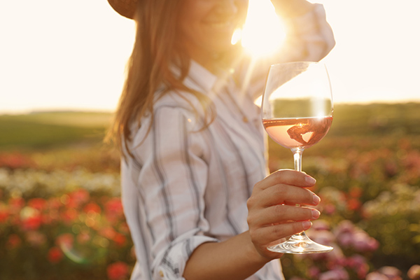 Woman with glass of wine in rose garden on sunny day