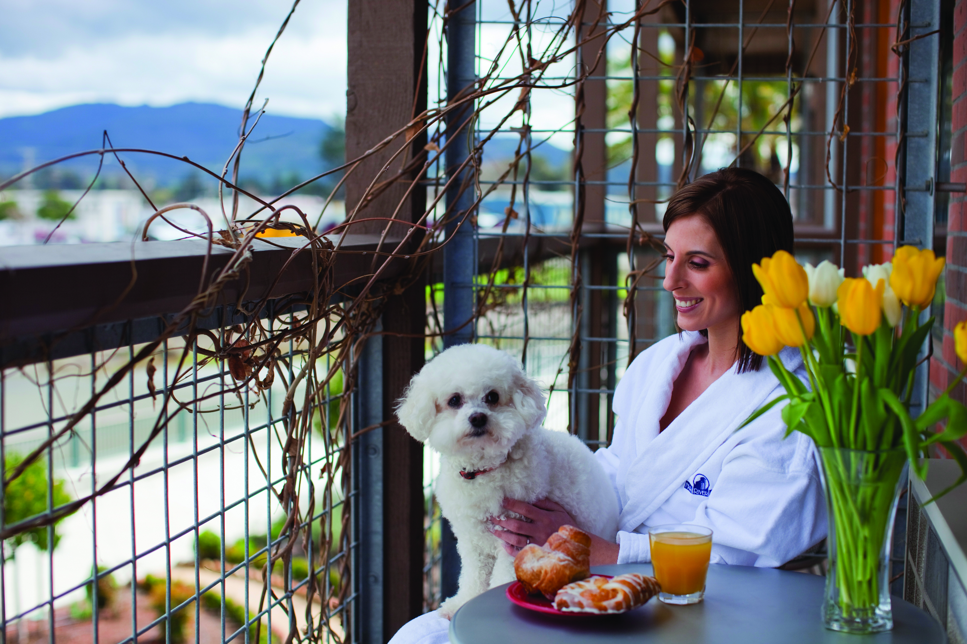 Woman in bathrobe sitting with dog on lap on balcony inside Napa River Inn