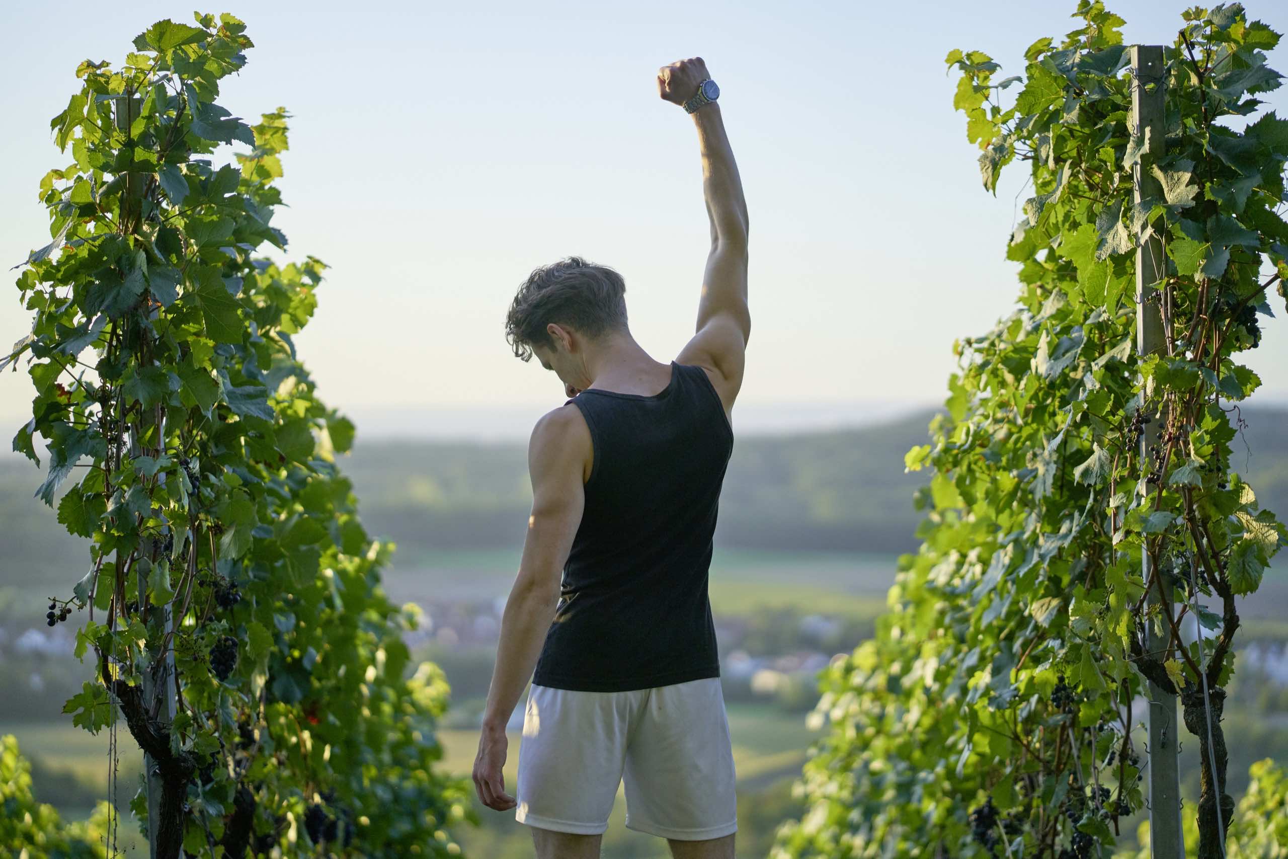 Runner raising his fist in celebration between vineyard rows in Napa.