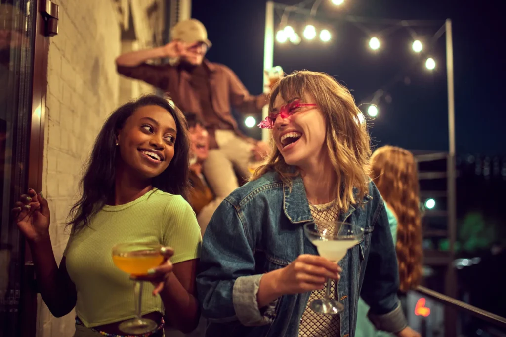 Friends enjoying cocktails and nightlife in Napa with playful pop concert energy and string lights overhead.